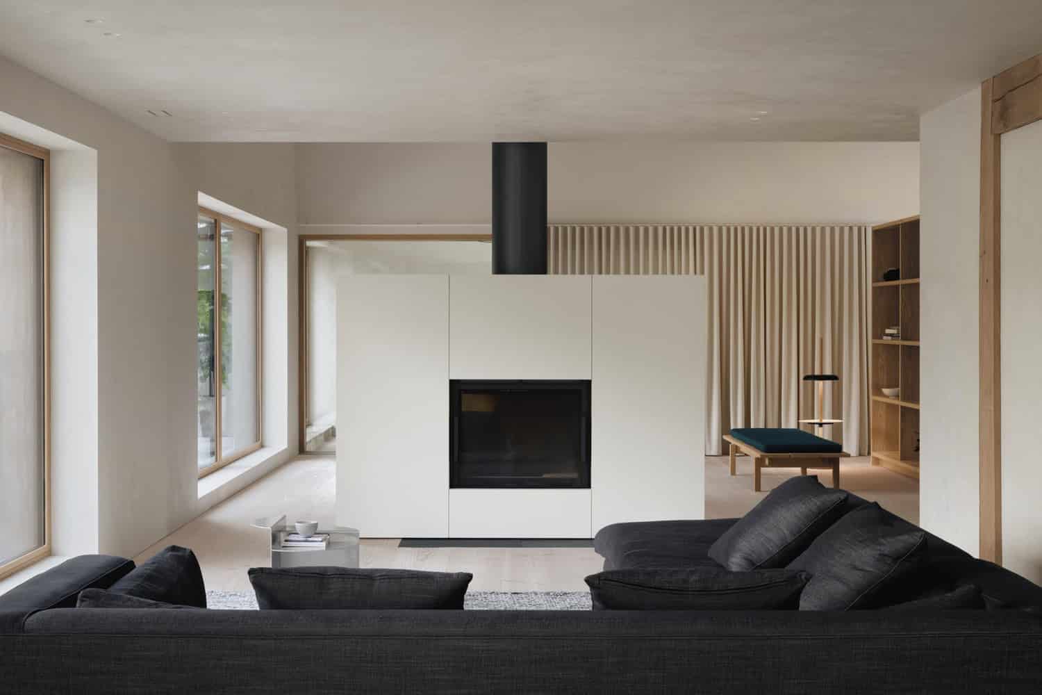 Maison Melba living room by Atelier L’Abri with central fireplace and dark modern sofa in Frelighsburg Quebec