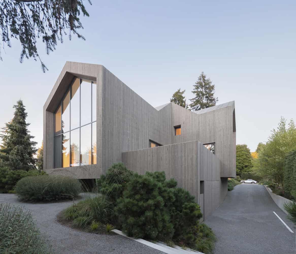 Modern minimalist concrete house with large glass windows, surrounded by lush greenery and natural landscape, showcasing contemporary architecture design.