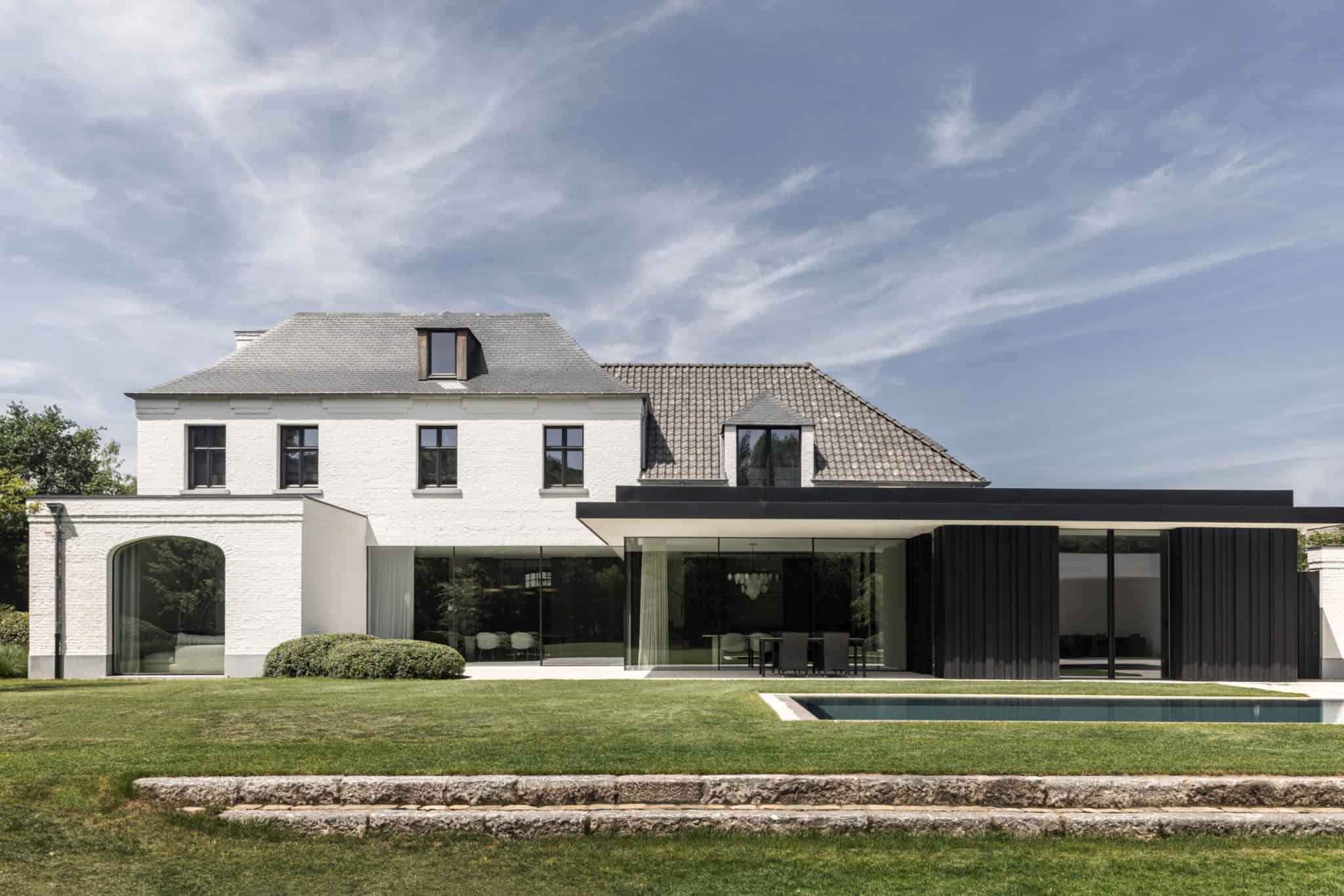 Modern luxury house with contemporary design, white brick facade, large glass windows, black accents, landscaped garden, and swimming pool, showcasing innovative architecture and elegant outdoor space.