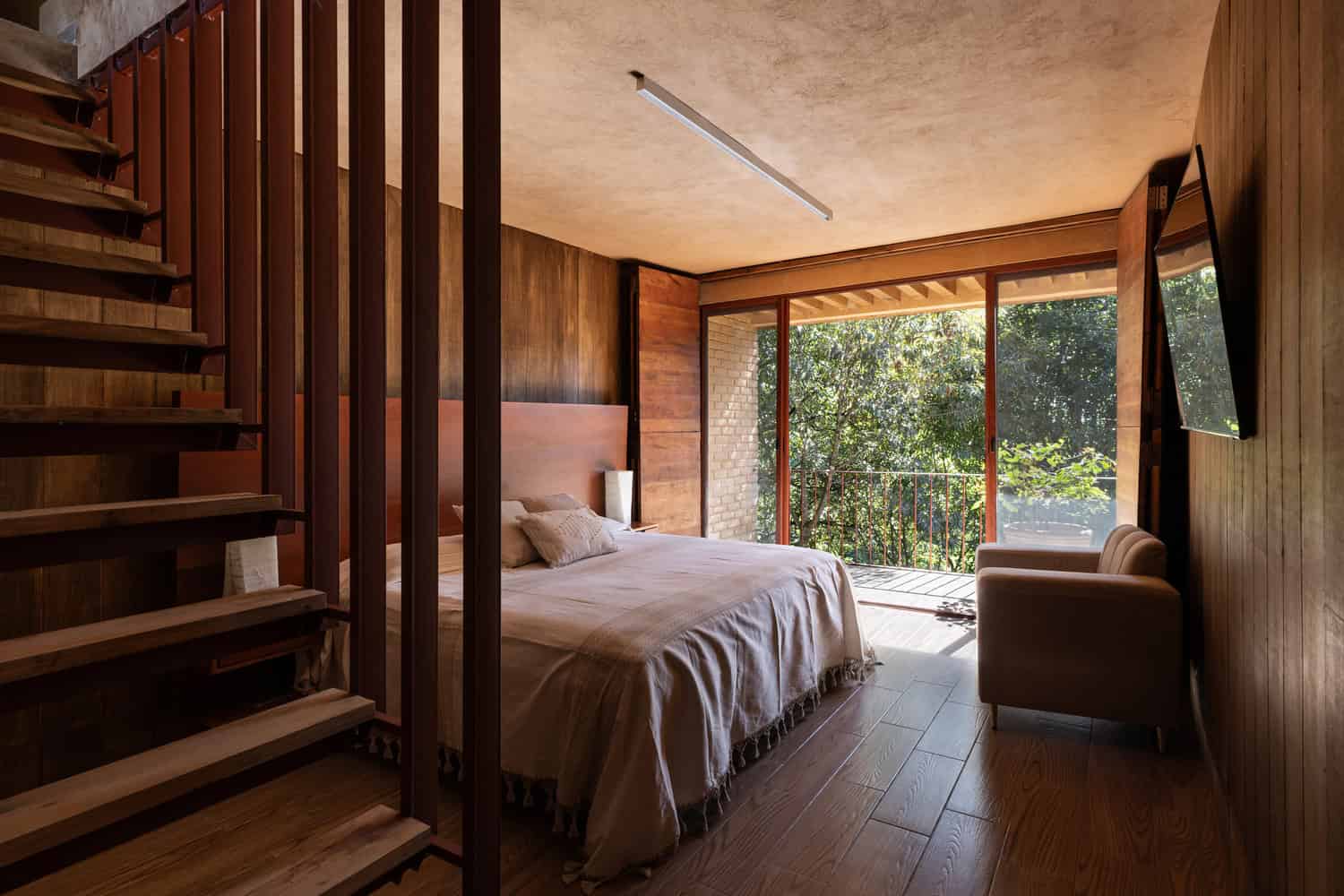 Intimate bedroom of The Sierra House by Valdez Arquitectos with adjacent staircase and balcony overlooking the forest in Chiapas, Mexico