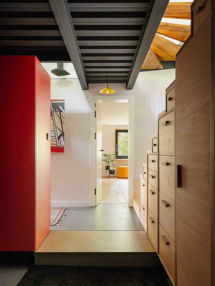 Vibrant modern entryway with bold red cabinet, natural wood storage, sleek dark ceiling, and contemporary artwork, showcasing stylish interior design and creative architectural use of space.