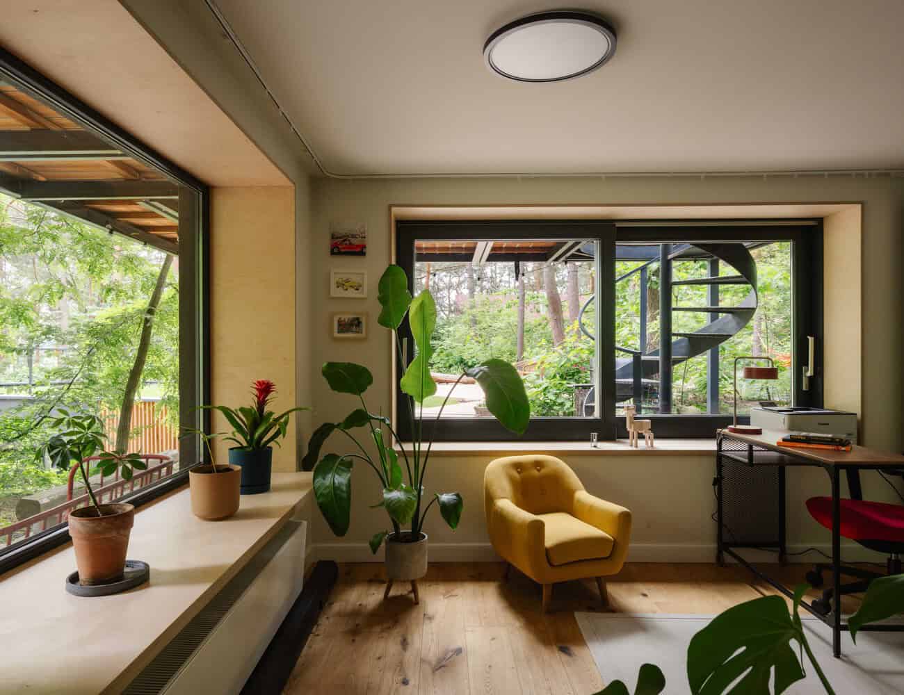 Bright interior with large windows showcasing a lush garden and spiral staircase, modern home design featuring indoor plants, cozy yellow armchair, and natural wood accents, emphasizing harmony with nature.