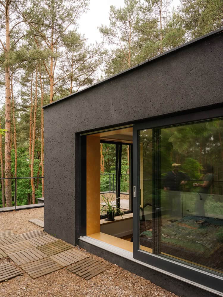 Contemporary black concrete tiny house with large sliding glass doors, set in a forest environment, showcasing modern architecture and eco-friendly design elements.
