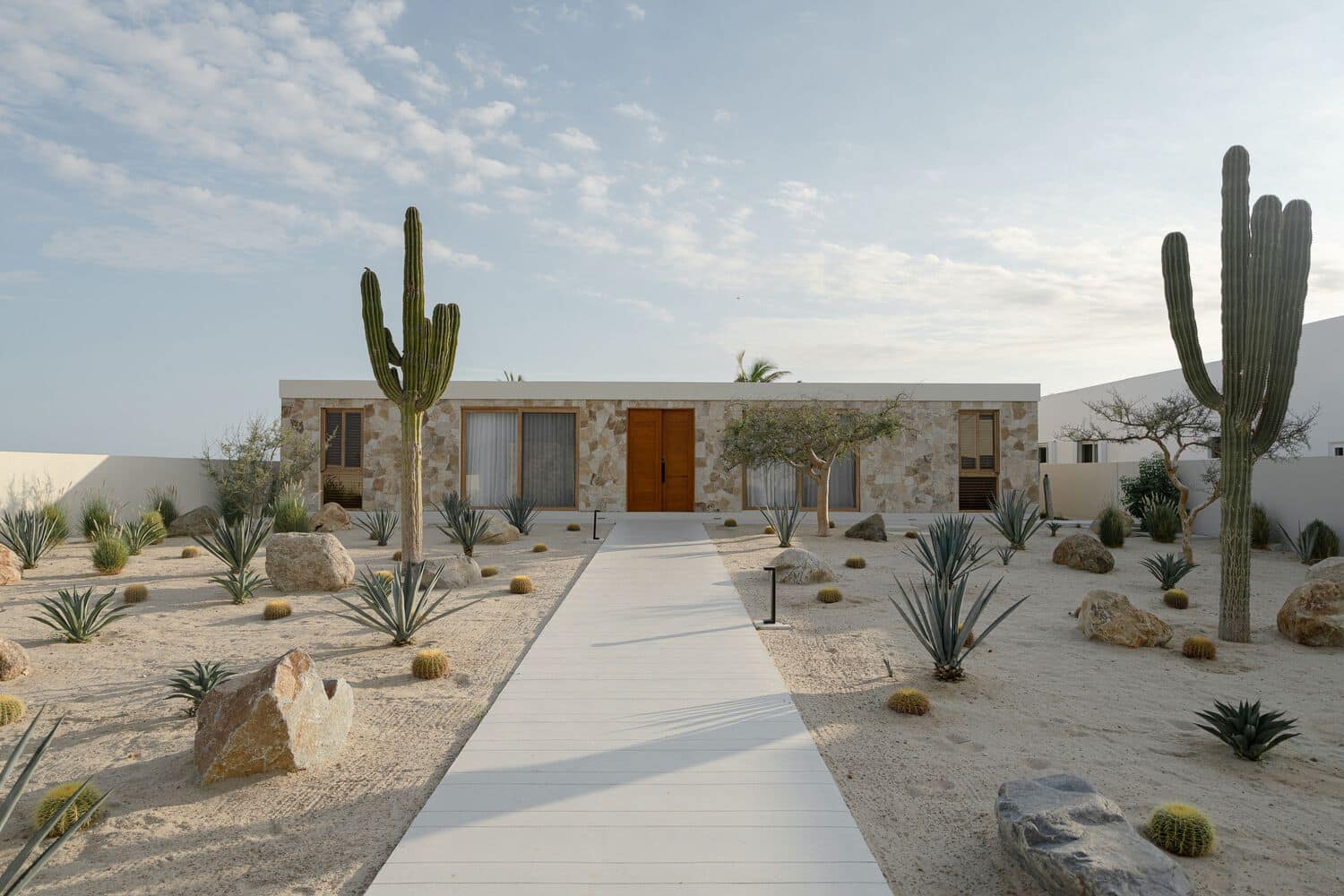 Desert landscape with modern minimalist house featuring desert plants and stone exterior, sunny sky, clean walkway, and natural materials for a stylish, sustainable architecture design.
