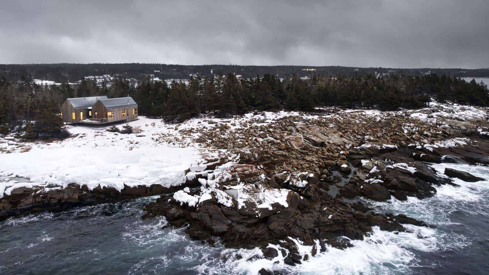 Aerial view of Tide Bound House by Peter Braithwaite Studio on a rocky, snow-covered Atlantic shoreline in Indian Harbour, Nova Scotia, Canada