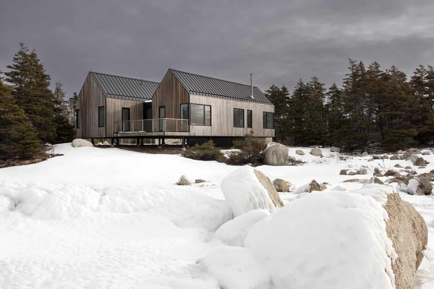 Angled exterior view of Tide Bound House by Peter Braithwaite Studio with raised deck and surrounding coastal forest in Indian Harbour, Nova Scotia, Canada