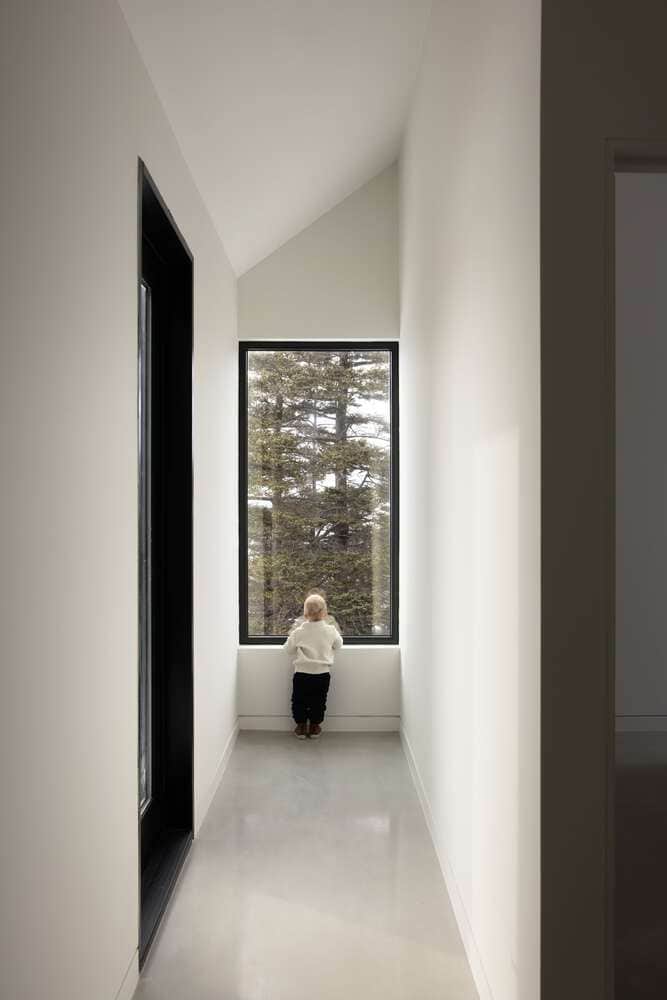 Minimal corridor interior inside Tide Bound House by Peter Braithwaite Studio with child looking through tall forest-view window