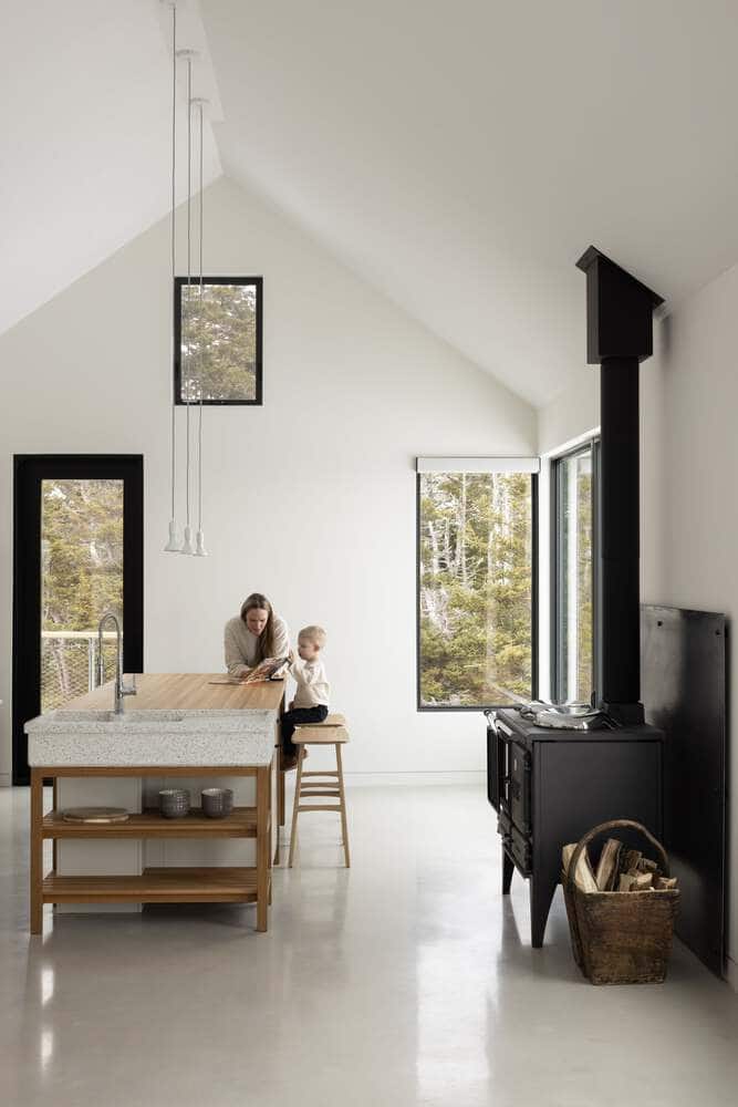 Kitchen interior of Tide Bound House by Peter Braithwaite Studio with family interacting beside the wooden island and forest-view windows