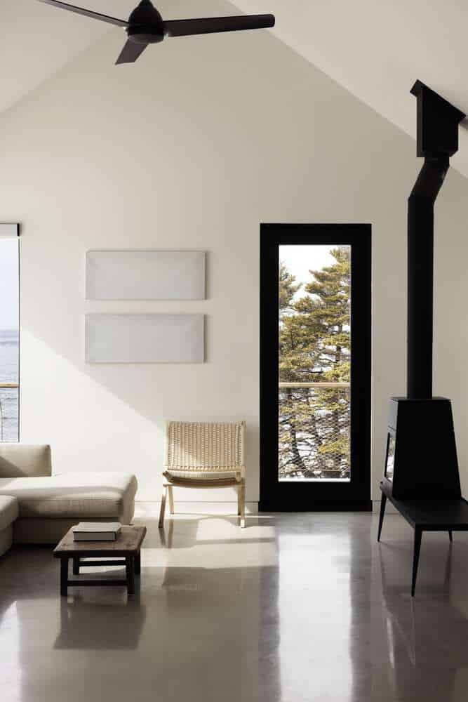 Living room of Tide Bound House by Peter Braithwaite Studio with minimalist furniture, wood stove and coastal views in Indian Harbour
