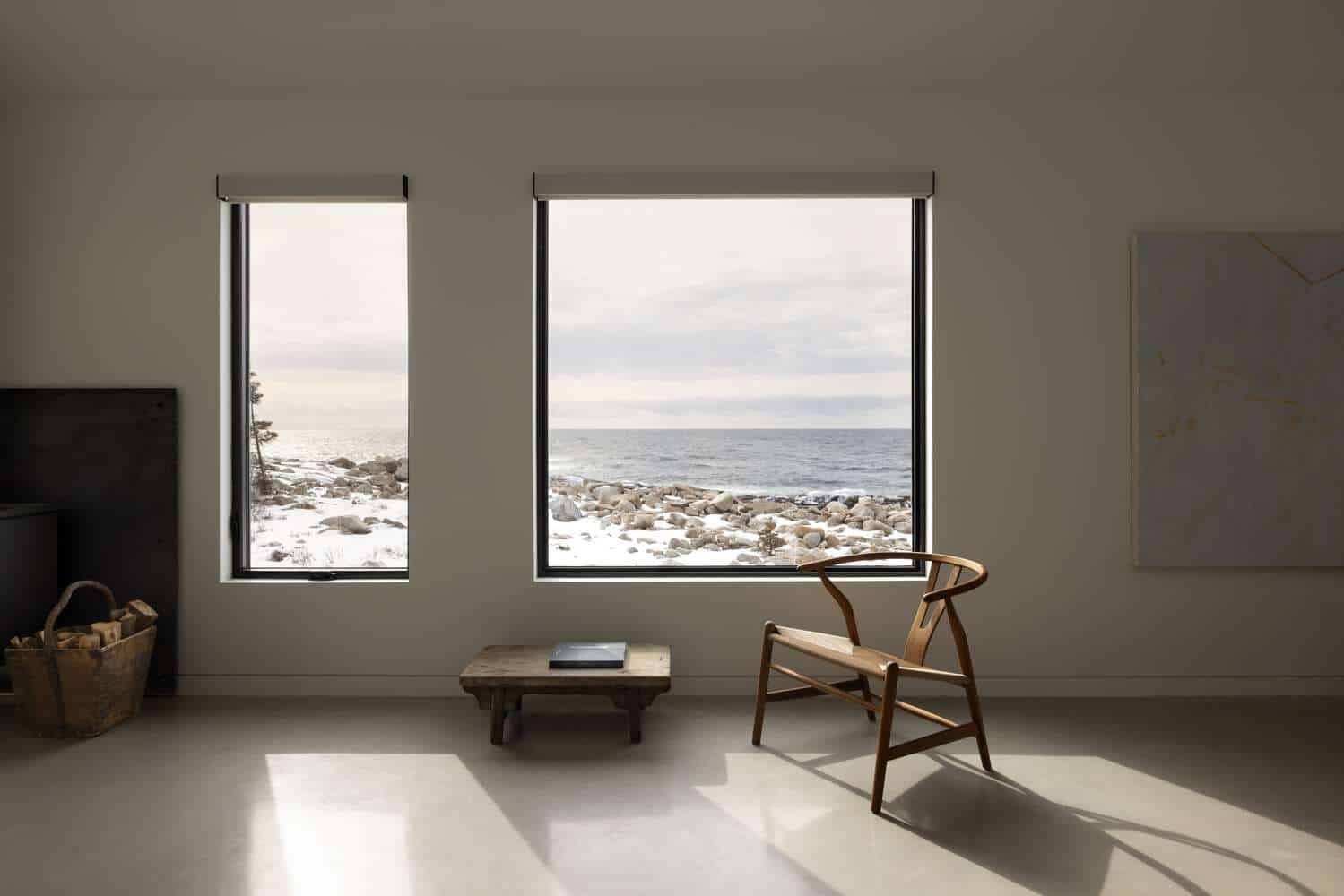 Interior view of Tide Bound House by Peter Braithwaite Studio showing large picture windows overlooking the snowy Atlantic coastline in Indian Harbour