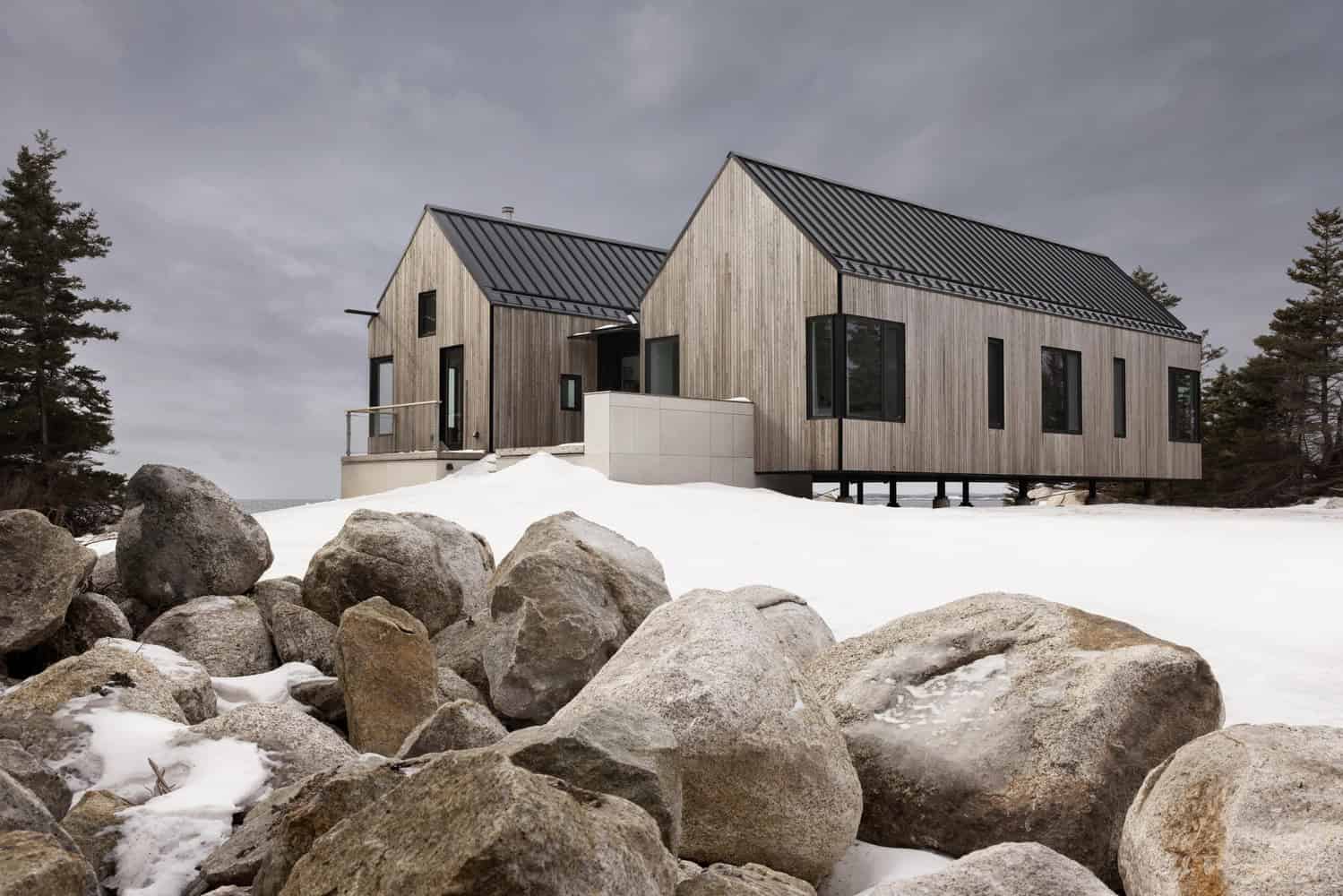 Oblique exterior view of Tide Bound House by Peter Braithwaite Studio with rocky shoreline and snow in Indian Harbour, Nova Scotia, Canada