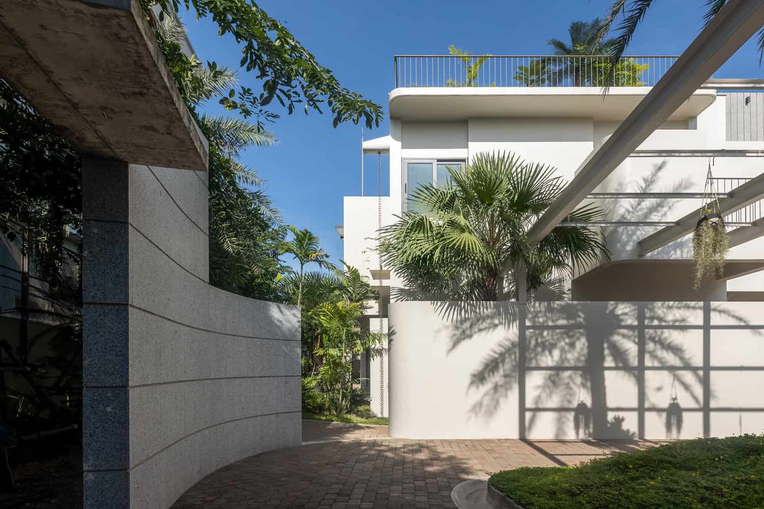 Wat Bo House by UAD Architects curved entry wall and driveway with palm shadows in Cambodia