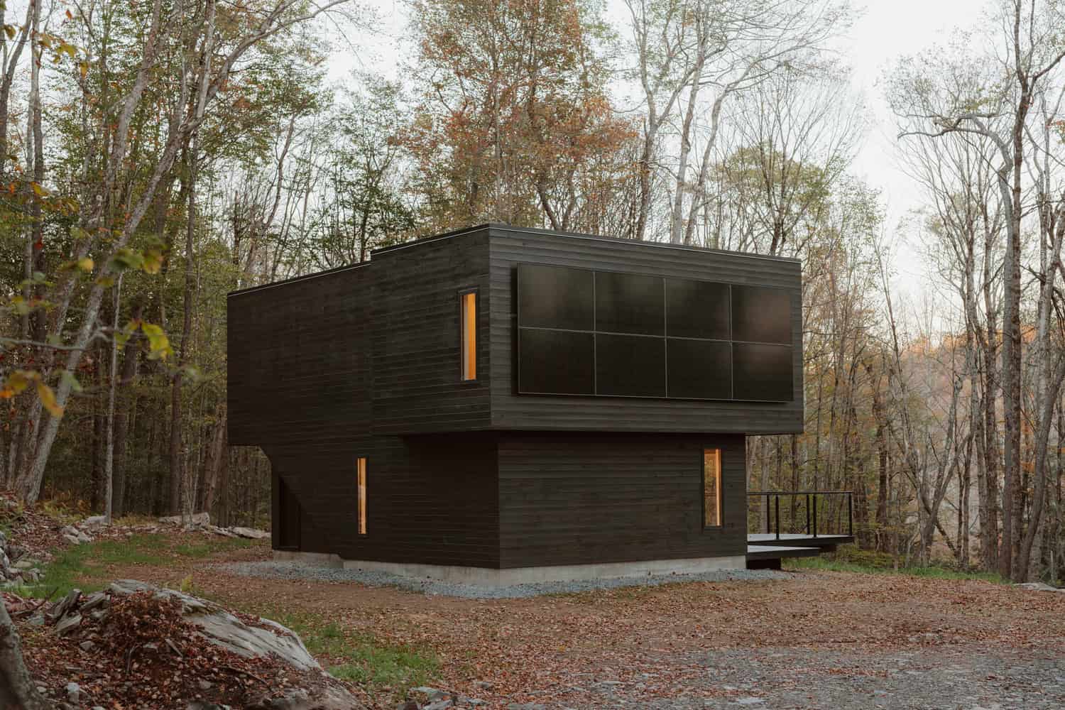 Contemporary black modern house in a forest setting with sleek design and large windows, showcasing innovative architecture and eco-friendly materials in a wooded environment.