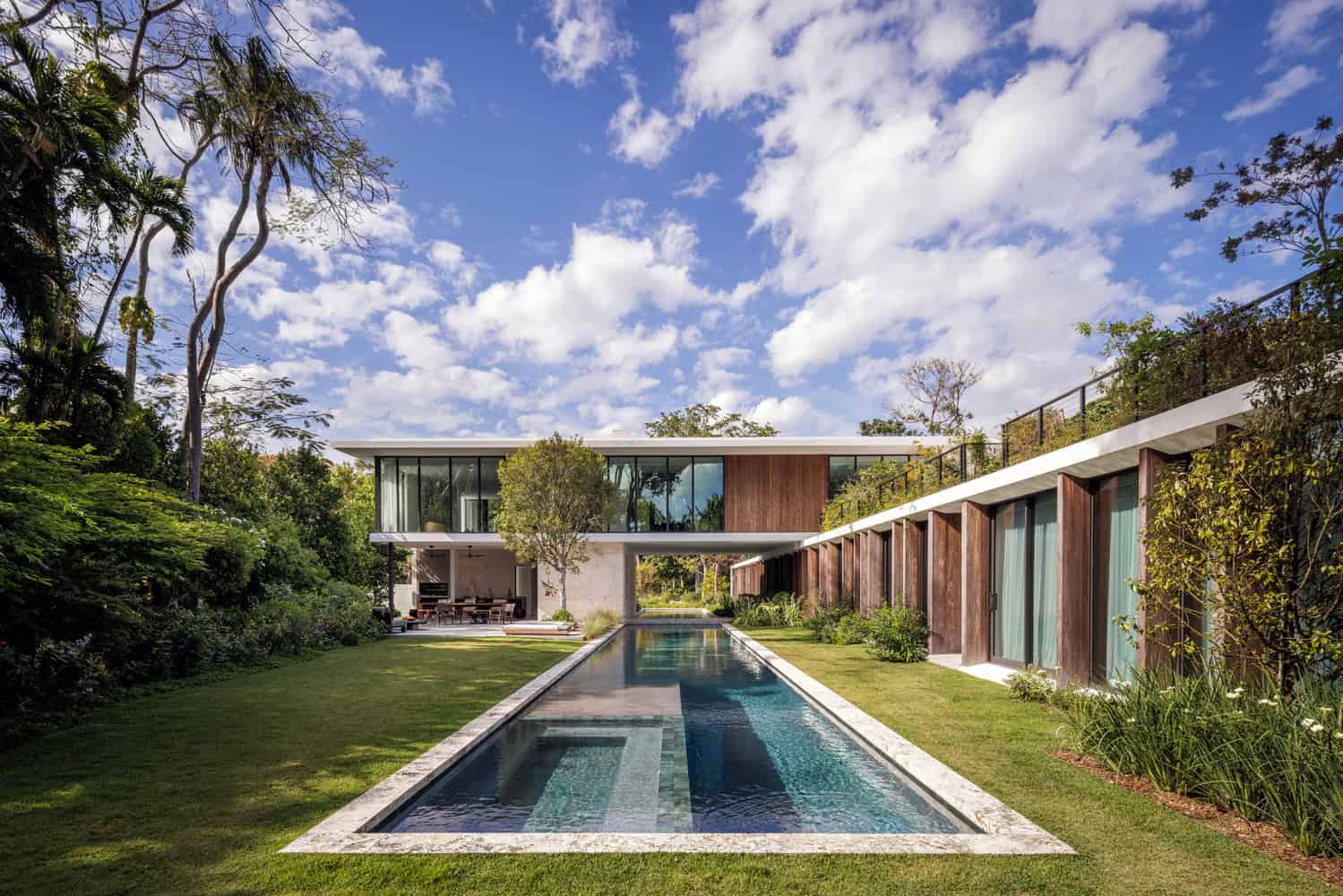 Modern luxury house with sleek design, glass walls, and outdoor pool in lush tropical garden, showcasing contemporary architecture art designs.