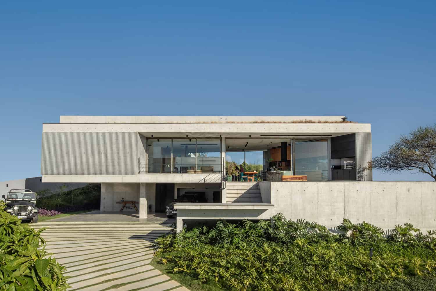 Modern minimalist concrete house with large glass windows, open-plan interior, and sleek design, featuring lush landscaping and a spacious driveway, exemplifying contemporary architecture and stylish home design.
