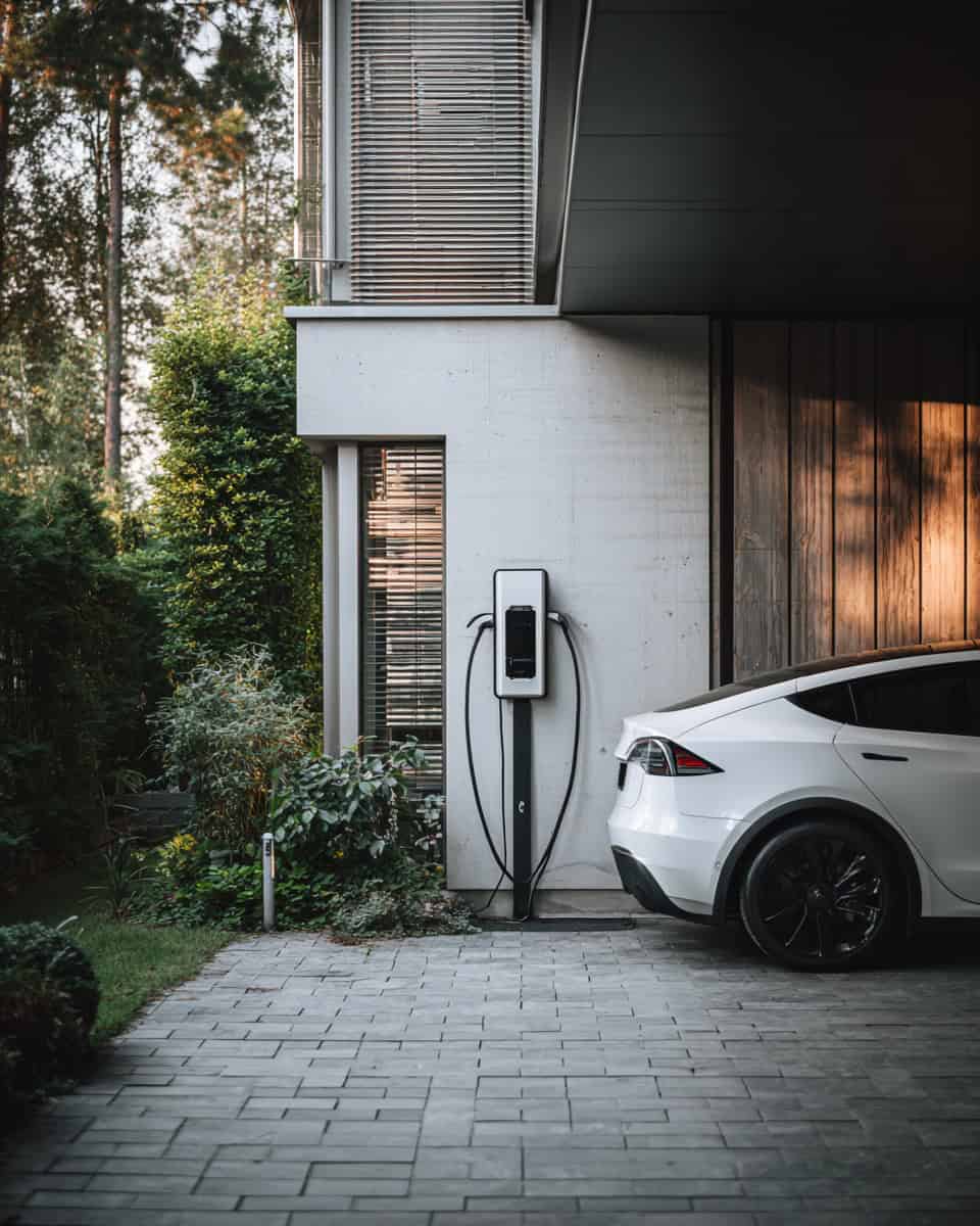 Electric vehicle charging station at modern home with white Tesla car, eco-friendly transportation, contemporary architecture, energy-efficient design, and outdoor landscape, showcasing sustainable living and innovative home technology.
