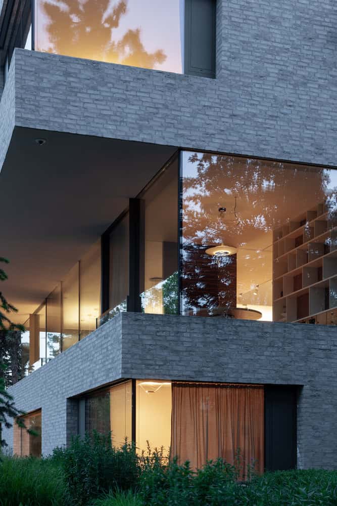 Villa Vista by Znameni Ctyr Architekti, corner library and living space with large glazed walls at dusk