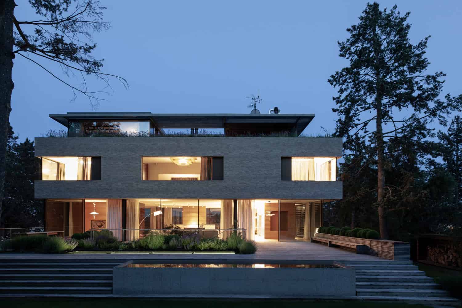 Villa Vista by Znameni Ctyr Architekti, front elevation at dusk with warm interior lighting and reflecting pool