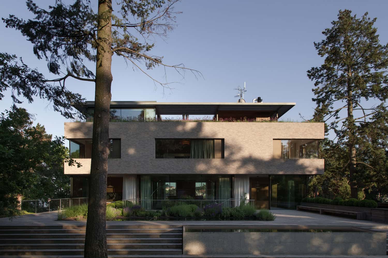 Villa Vista by Znameni Ctyr Architekti, front elevation with tall trees casting shadows