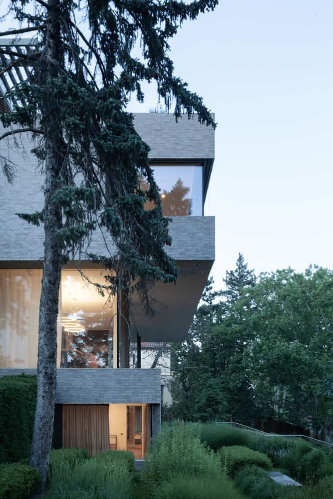 Villa Vista by Znameni Ctyr Architekti, side elevation at dusk framed by tall trees and layered volumes