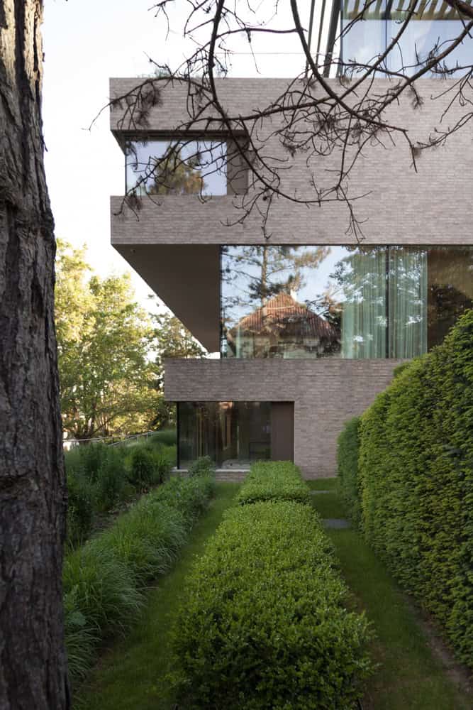 Villa Vista by Znameni Ctyr Architekti, narrow side garden path with hedges and cantilevered brick volume
